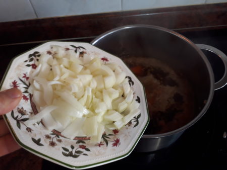 Añadiéndole la cebolla troceada a la olla